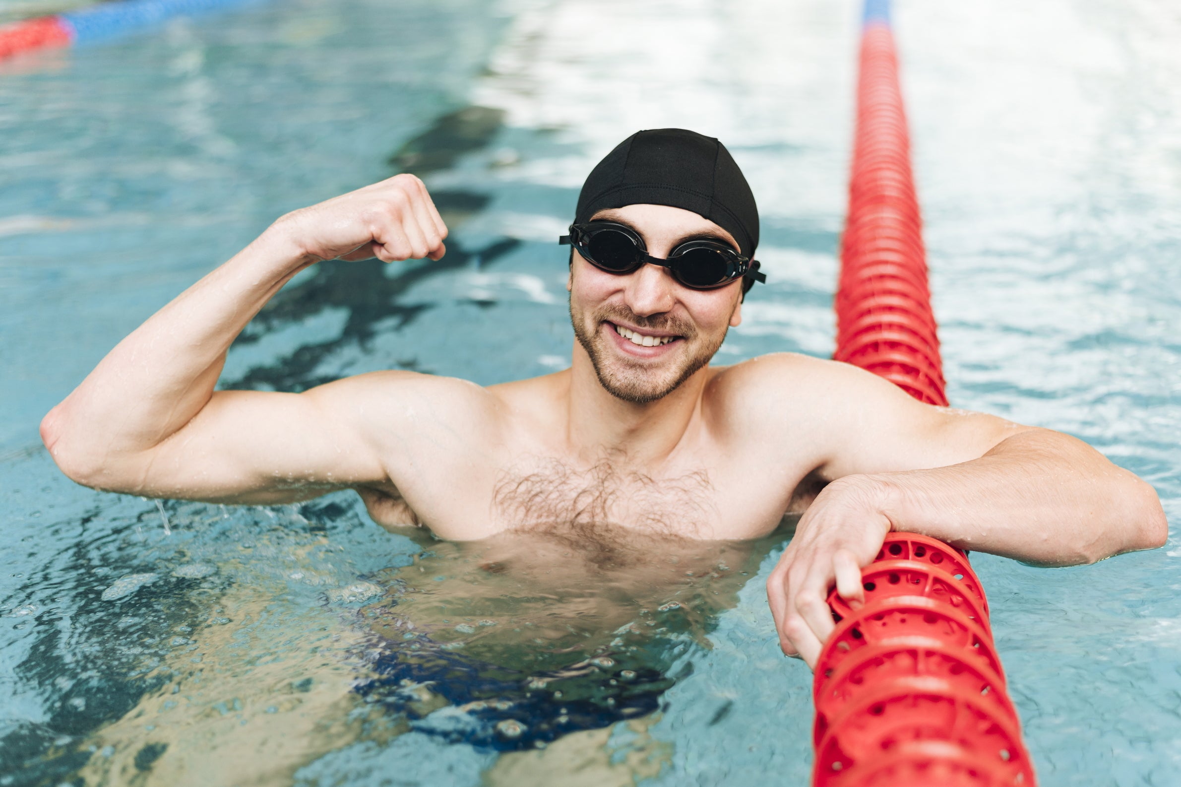 Männlicher Schwimmer der lächelnd seine Muskeln zeigt