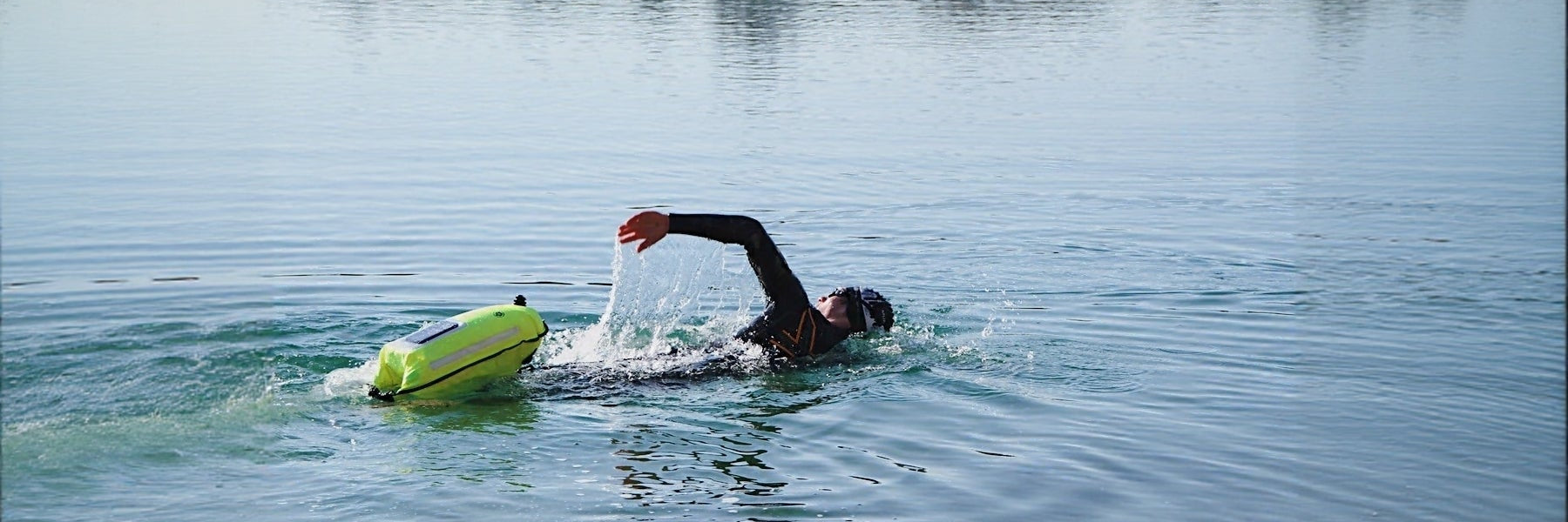 Ein Mann im Neoprenanzug schwimmt im See und zieht eine neongelbe Schwimmboje hinter sich her