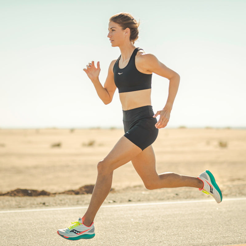 Eine Läuferin in kurzer Laufbekleidung beim Tempolauf auf einer einsamen Straße, Ansicht von der Seite
