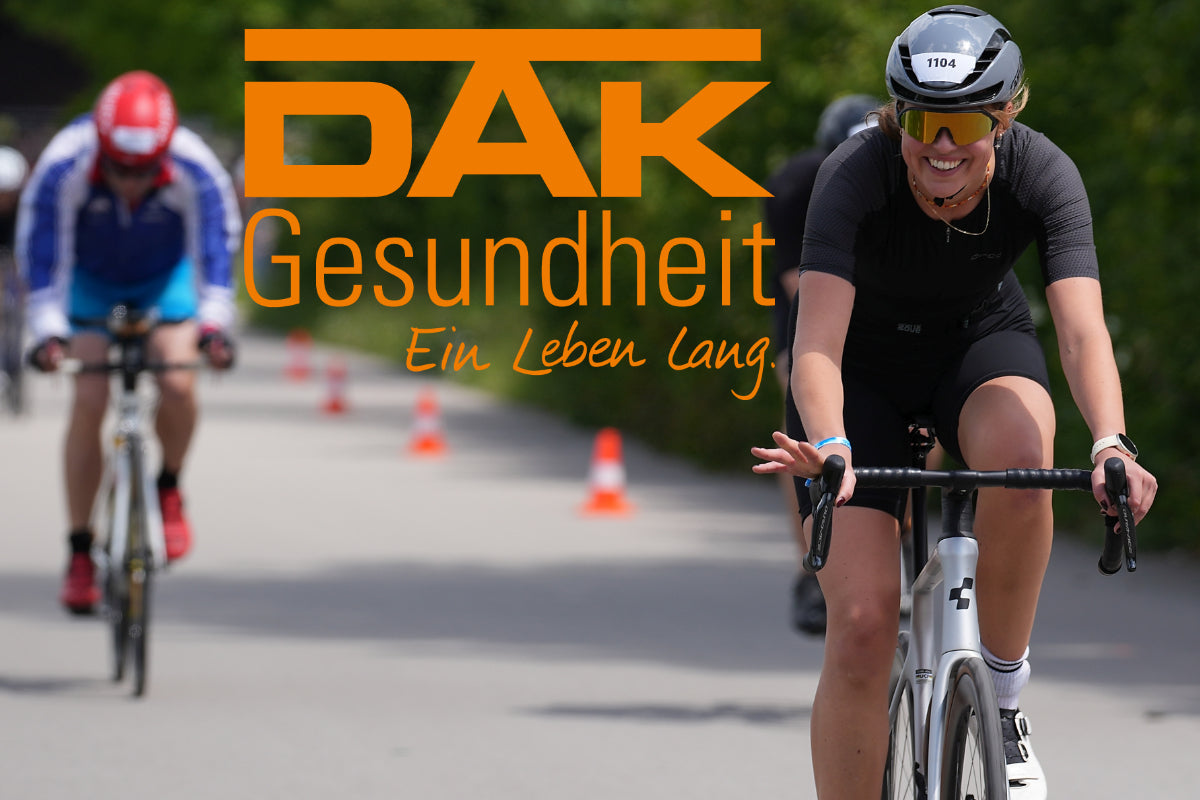 Titelbild: eine Radfahrerin auf dem Rennrad  von vorn lächelt in die Kamera. Daneben das DAK Logo 