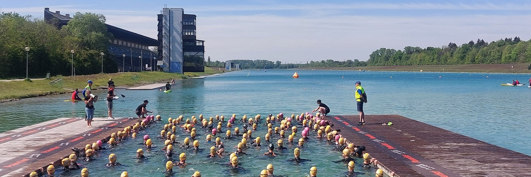 Triathleten mit gelben Badekappen warten im Wasser der Ruderregattastrecke Oberschleissheim  auf den Start