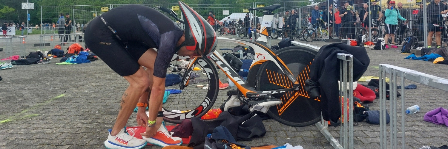 Ein Triathlet in der Wechselzone hat sein Fahrrad abgestellt und schlüpft in seine Laufschuhe 